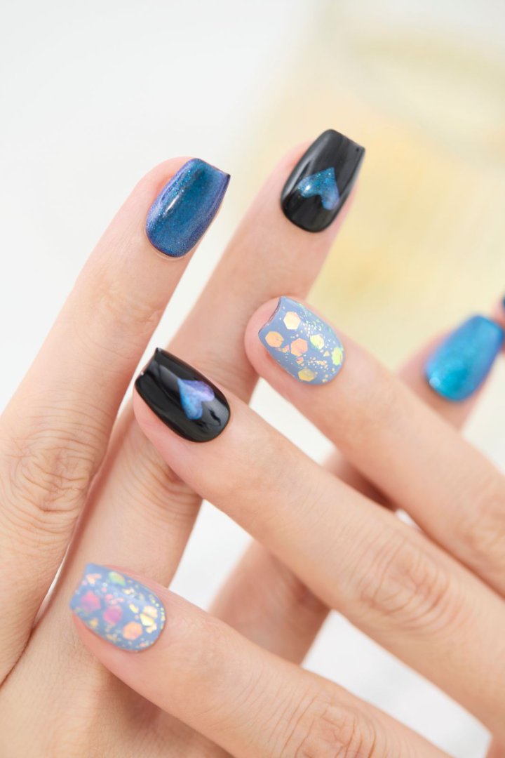 「ブルーマグネット×ブラックハートのジェルネイルチップを指先に着けた手元アップ。オーロラフレークのブルーネイルが光に輝くリユーザブルネイルデザイン」